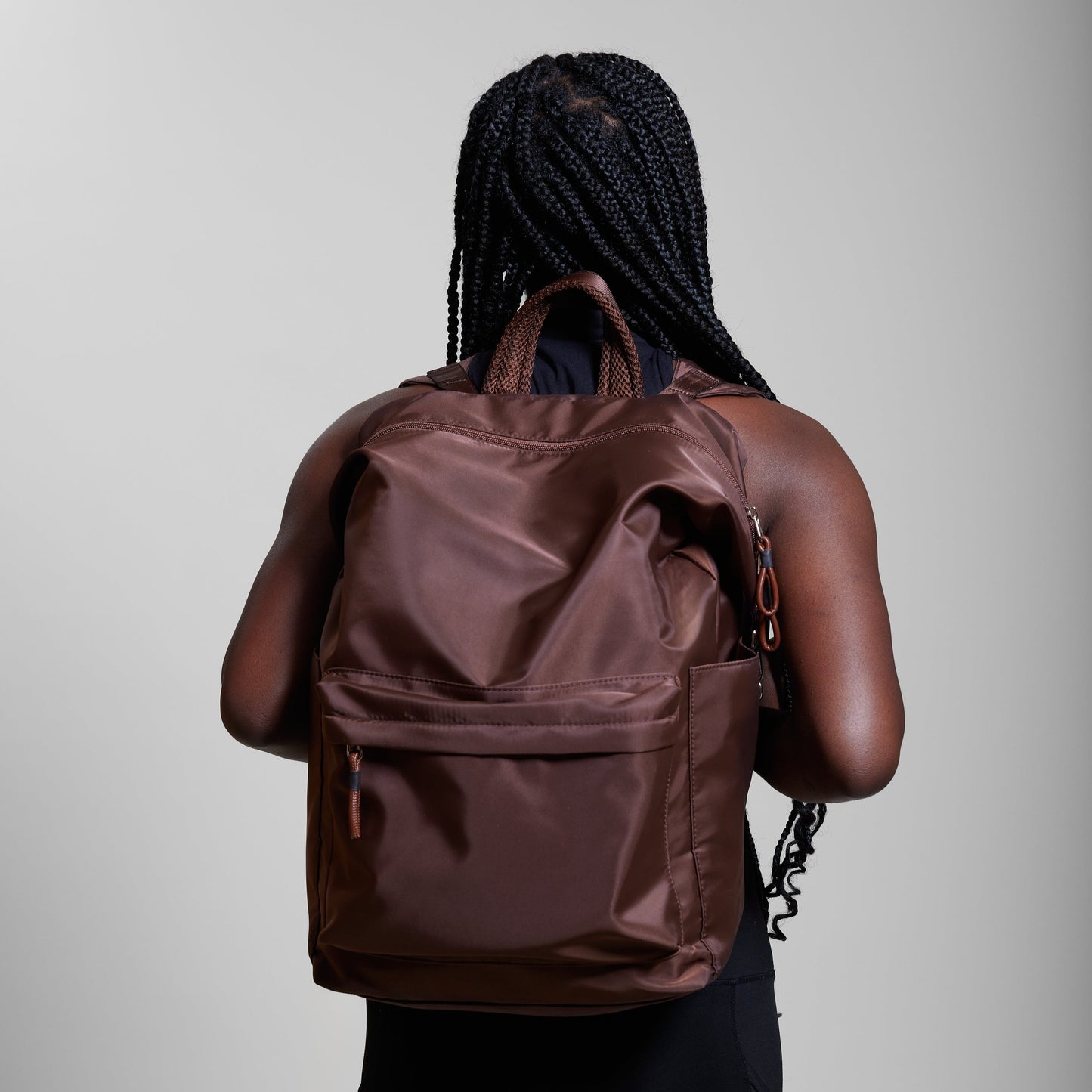 Female model wearing Karma Woodland Brown Backpack as a backpack. Backpack has a top handle and a convertible strap to carry your backpack as a tote for easy grab and go!
